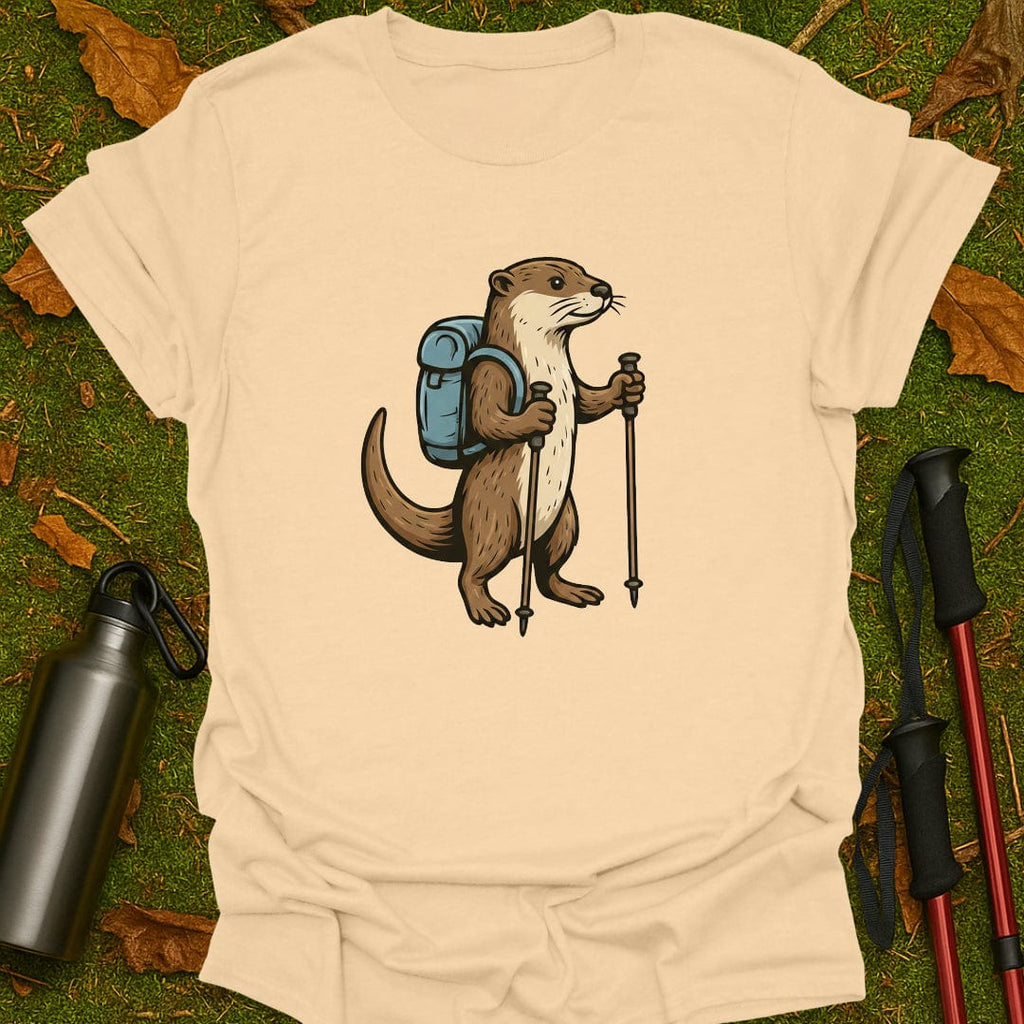 Beige t-shirt with an otter illustration holding hiking poles and a backpack on a grassy background.