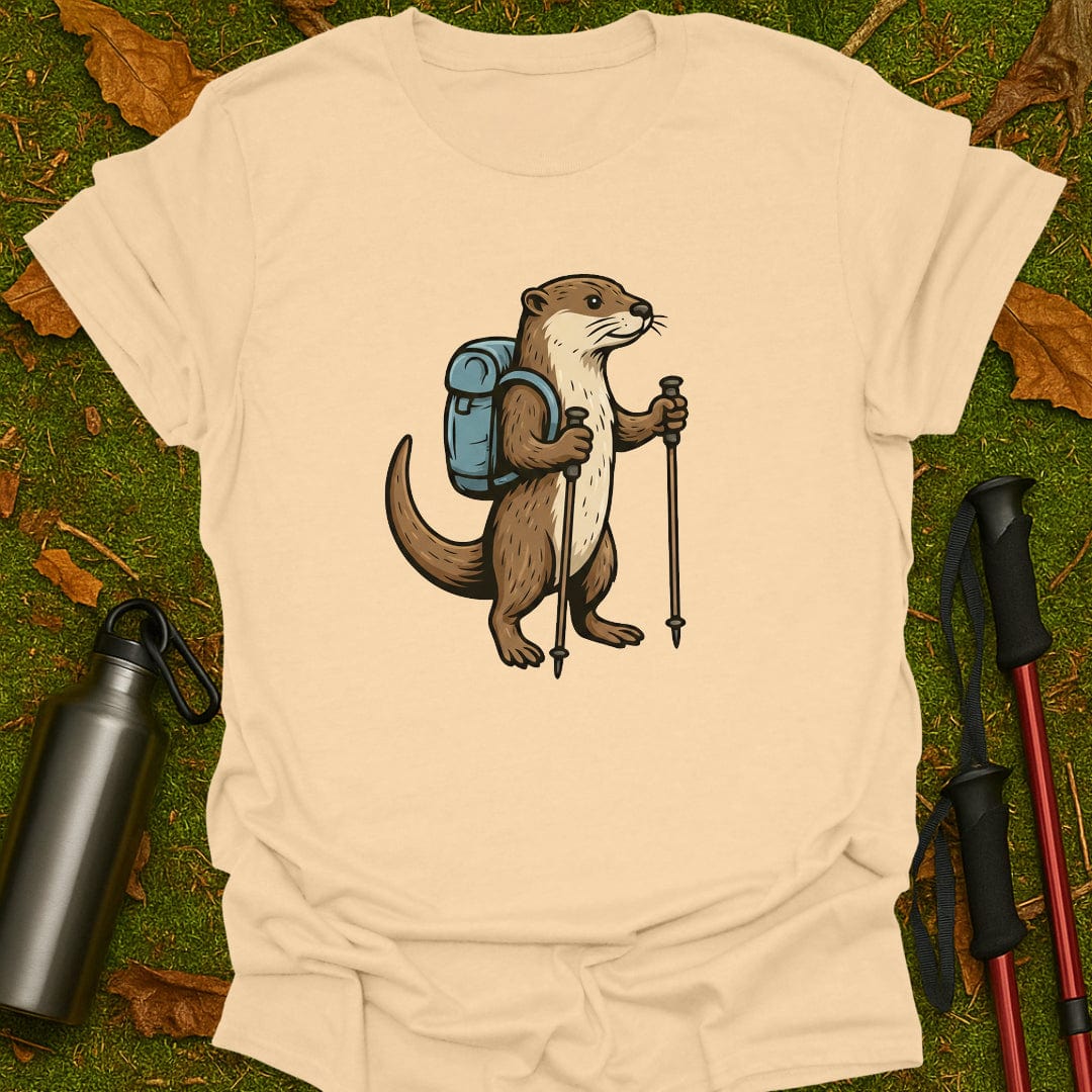 Beige t-shirt with an otter illustration holding hiking poles and a backpack on a grassy background.
